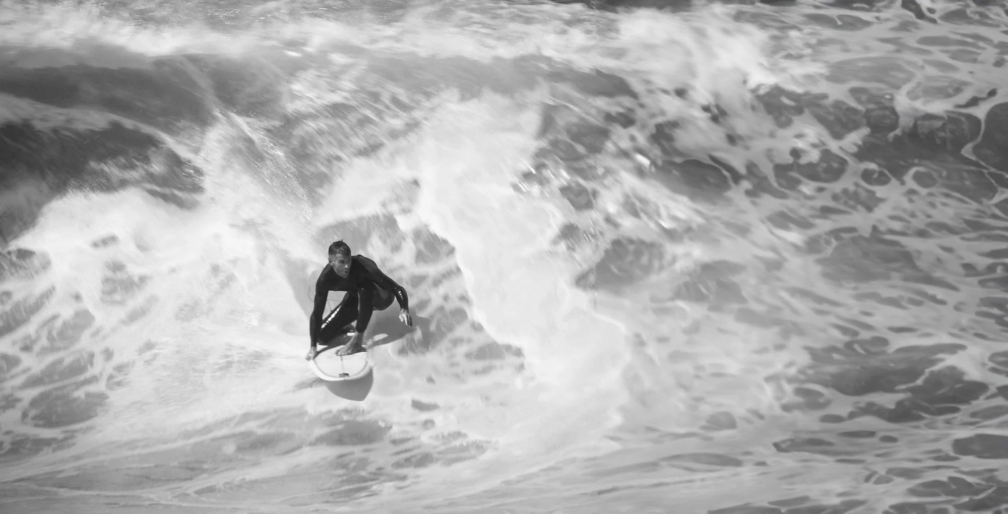 Person surfing with hexagonal surf grip packs on a large wave in black and white.