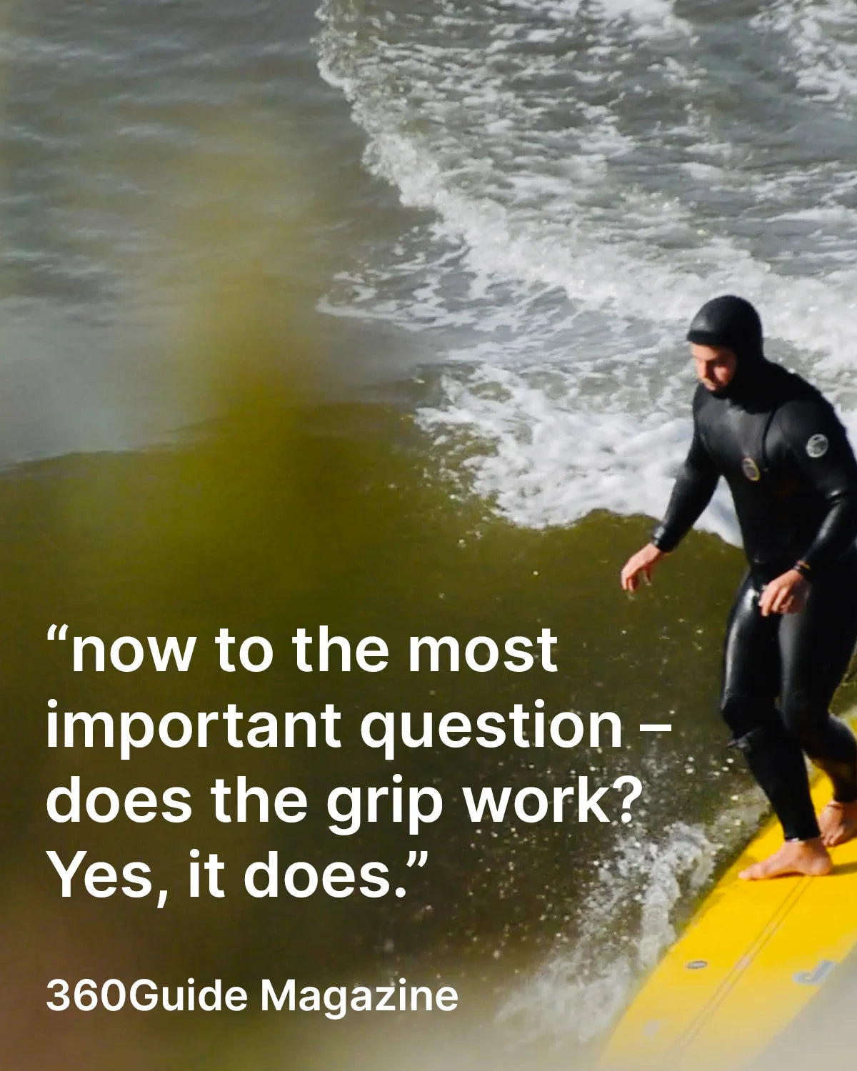 Person in a wetsuit standing on a yellow longboard with front grip pads